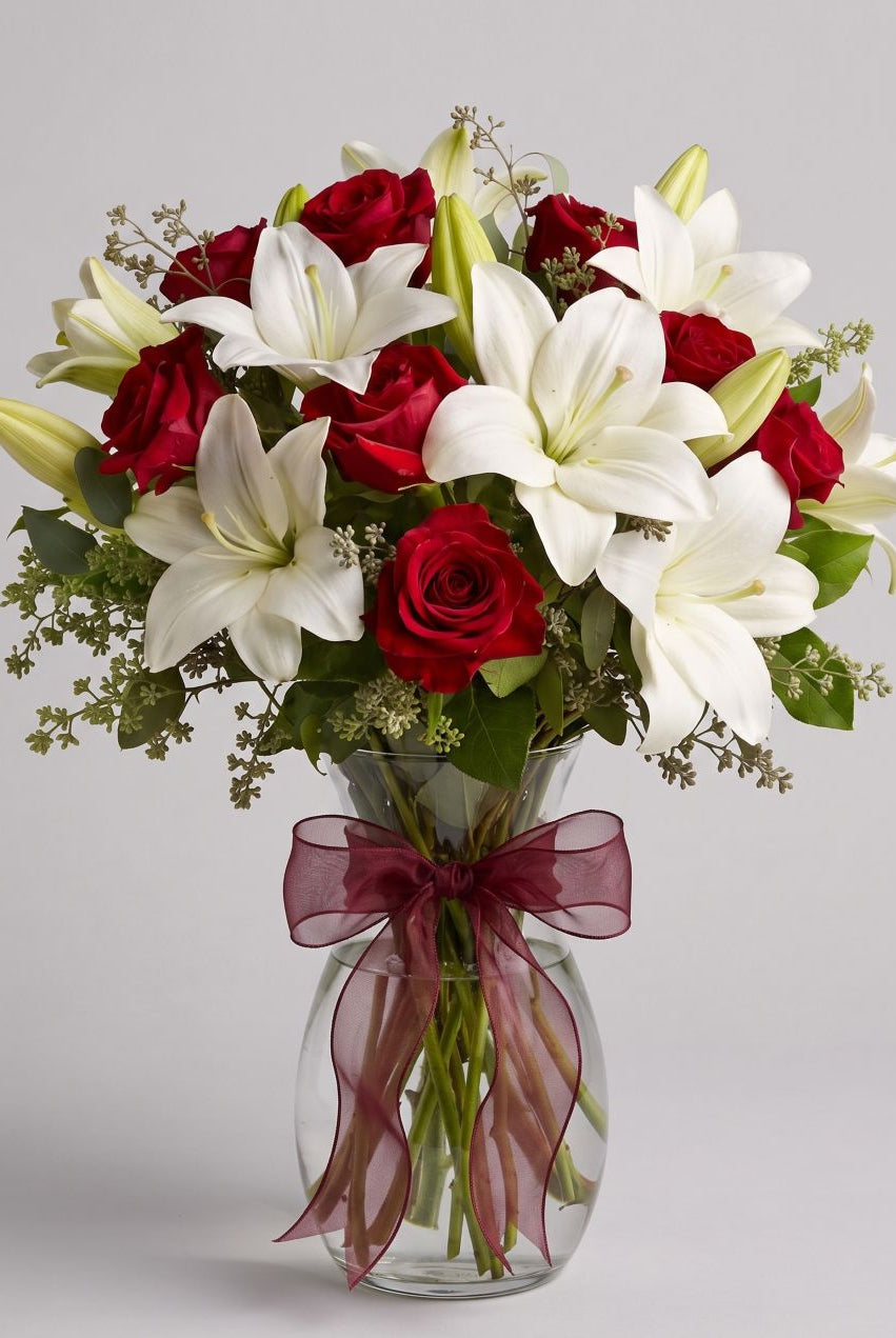 Baby Be Mine arrangement of red roses, white lilies and seeded eucalyptus in a clear glass vase with a burgundy organza bow