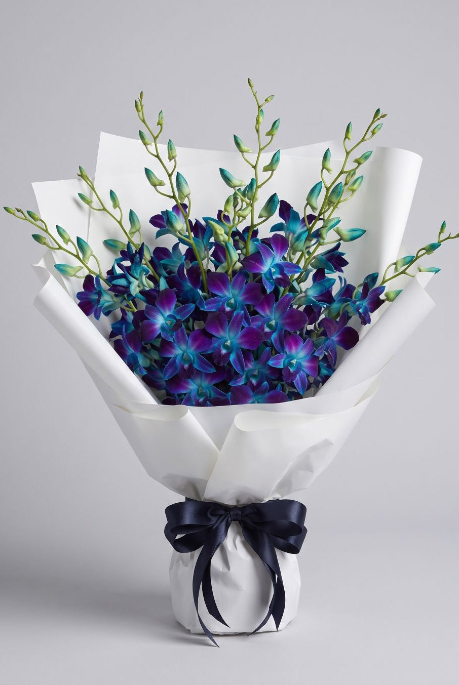 Blue Dendrobium Bouquet of blue and violet dendrobium orchids with turquoise buds wrapped in white paper with a navy satin ribbon