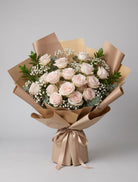 18 Dusty Ivory Roses Bouquet of eighteen blush-ivory Quicksand roses with baby’s breath, eucalyptus and greenery wrapped in champagne and tan paper with a champagne satin ribbon