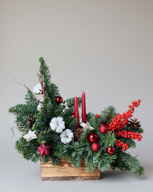 Decorative Christmas arrangement with greenery, red berries, and candles.