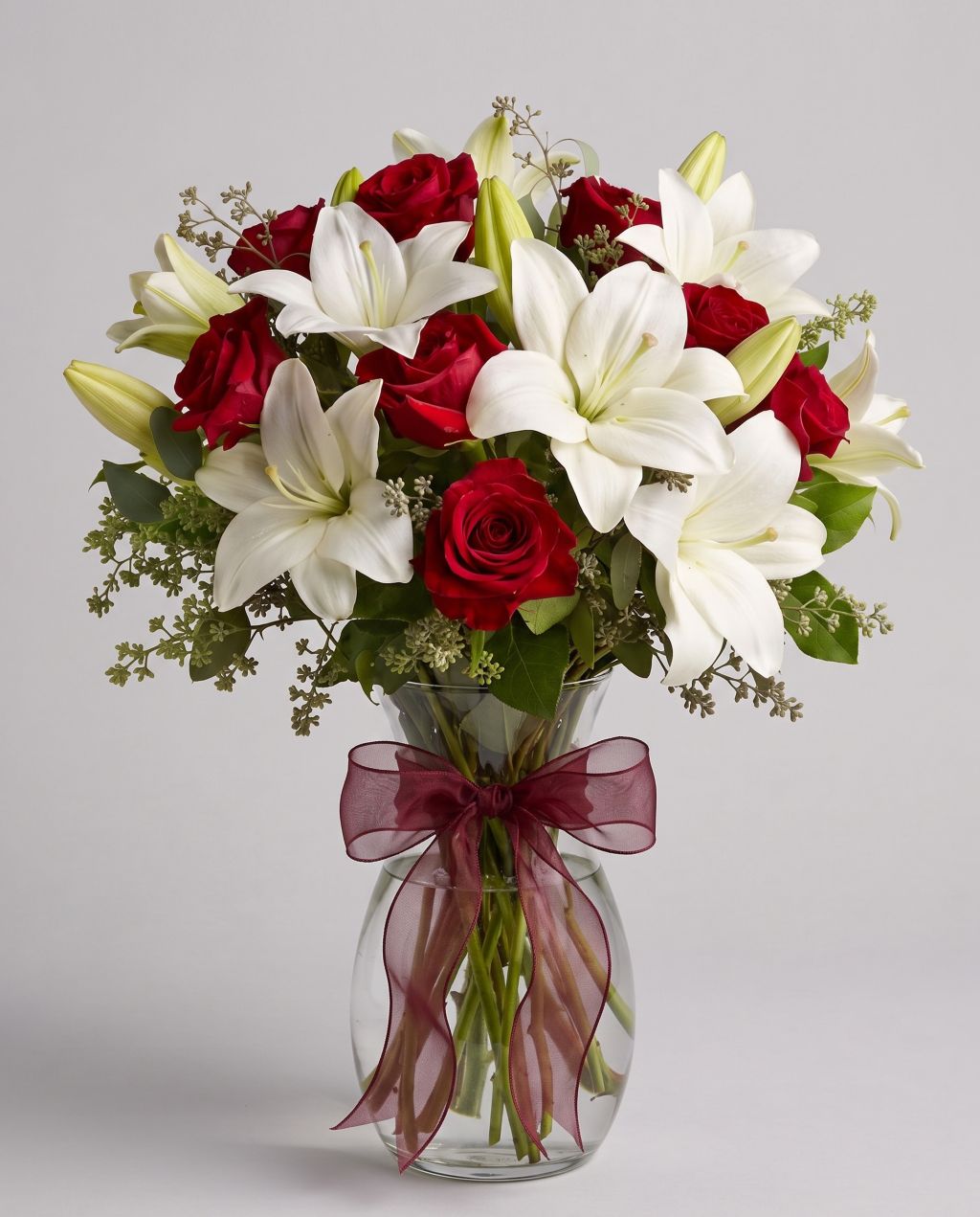 Baby Be Mine arrangement of red roses, white lilies and seeded eucalyptus in a clear glass vase with a burgundy organza bow