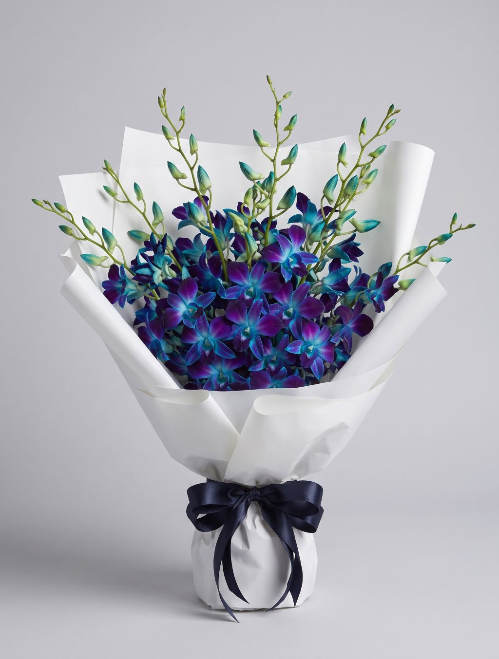 Blue Dendrobium Bouquet of blue and violet dendrobium orchids with turquoise buds wrapped in white paper with a navy satin ribbon