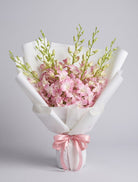 Blush Dendrobium Bouquet of soft pink and white dendrobium orchids with green buds wrapped in white paper with a pink satin ribbon