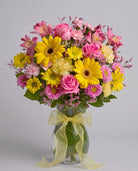Dazzling Day arrangement of yellow gerbera daisies, pink roses, pink alstroemeria, carnations and asters in a leaf-lined glass vase with a yellow bow