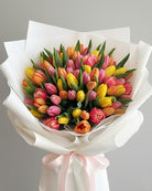 Bouquet of colorful tulips wrapped in white paper with a pink ribbon on a gray background