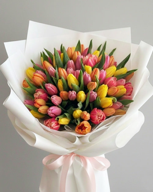 Bouquet of colorful tulips wrapped in white paper with a pink ribbon on a gray background