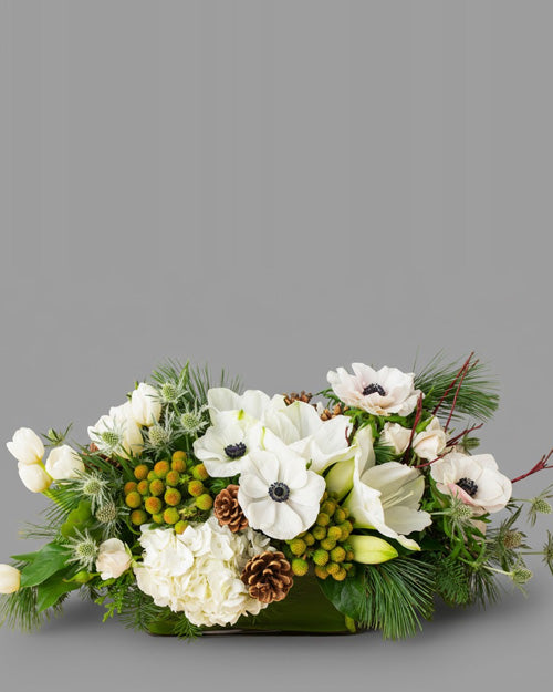 The Holiday Treasure arrangement, a lush centerpiece with red amaryllis and gold accents on a festive dining table.