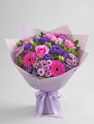 Seasonal Pinks & Purples Bouquet of hot pink roses, pink gerbera daisies, purple lisianthus, lavender daisy mums and purple statice wrapped in lavender paper with a lavender ribbon