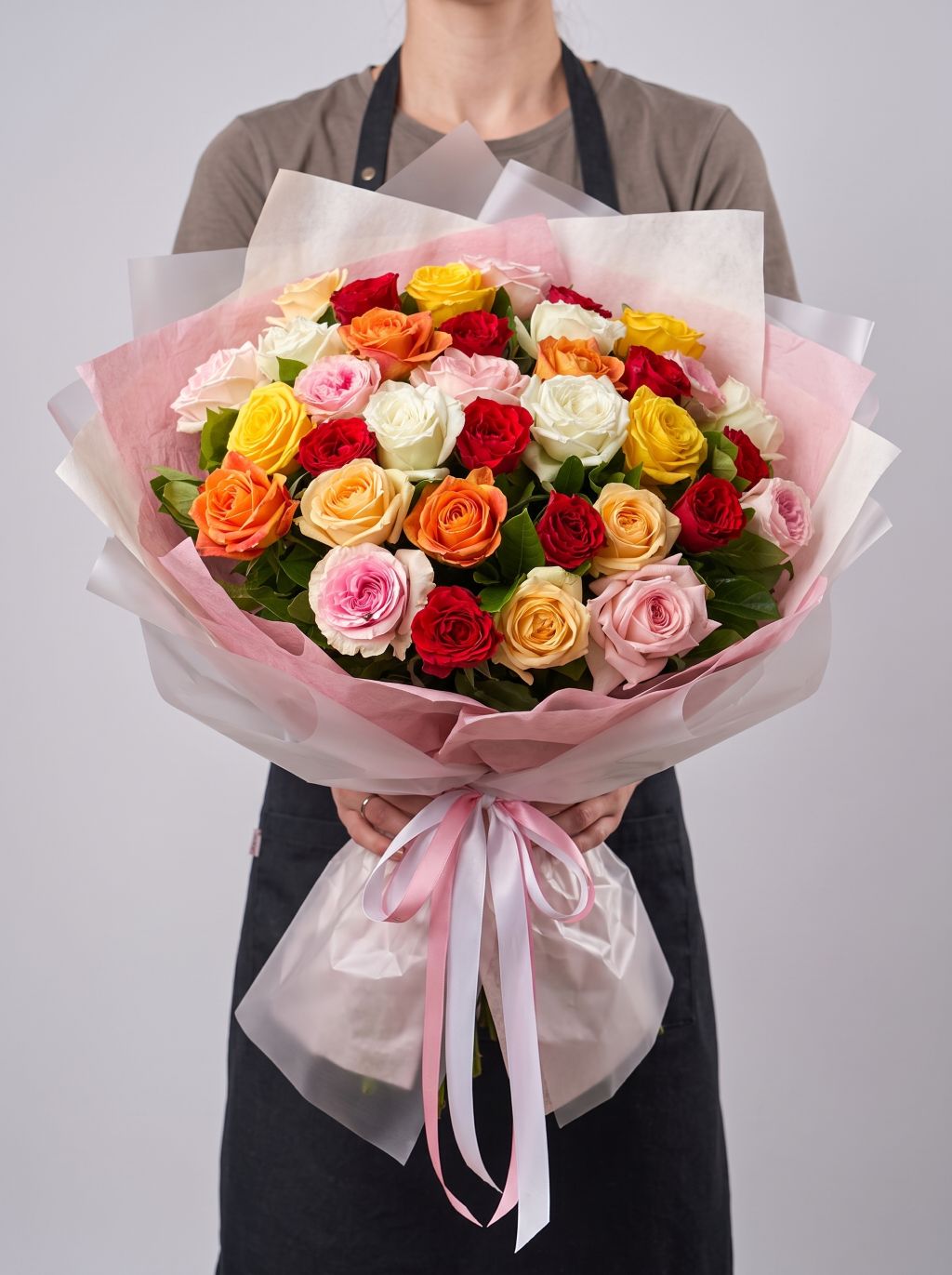 Sunset Fiesta Roses bouquet of mixed red, pink, peach, orange, yellow and white roses wrapped in clear cellophane with pink ribbon
