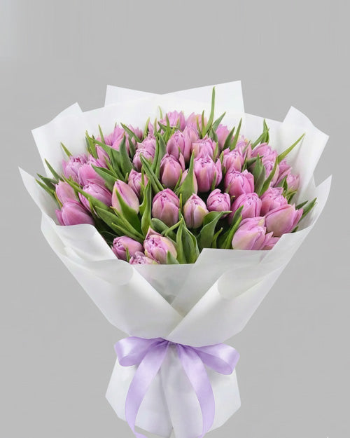 Bouquet of pink tulips wrapped in white paper with a purple ribbon on a gray background