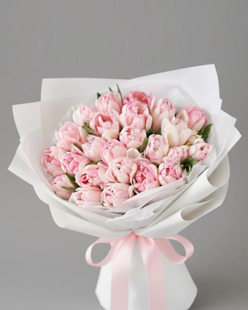 Bouquet of pink tulips wrapped in white paper with a pink ribbon on a gray background