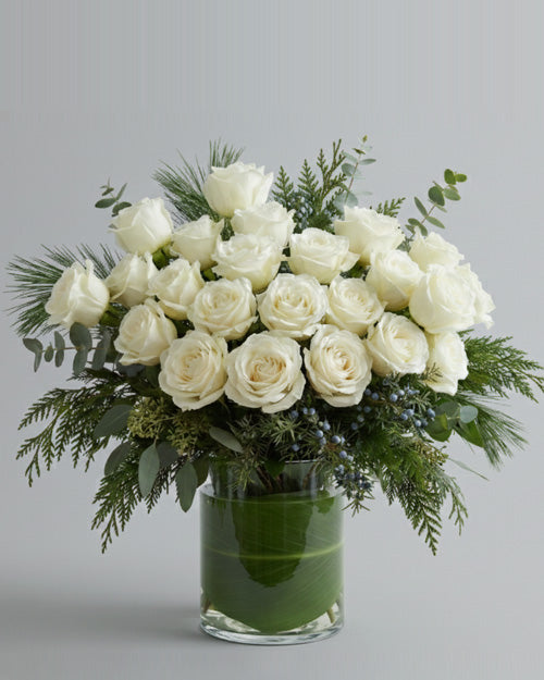 Bouquet of white roses with greenery in a clear vase on a light gray background
