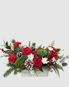 Floral arrangement with red roses, greenery, and pinecones in a white container on a white background