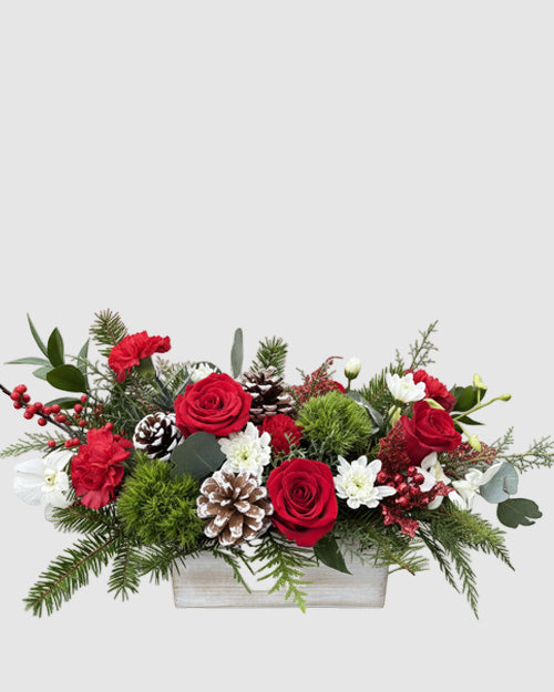Floral arrangement with red roses, greenery, and pinecones in a white container on a white background