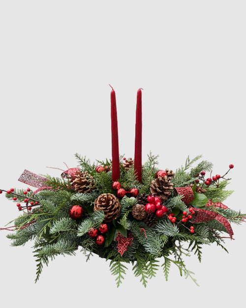 Decorative Christmas arrangement with red candles, pine cones, and berries on a white background
