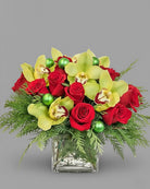 Bouquet of red roses, yellow orchids, and green ornaments in a clear glass vase on a gray background